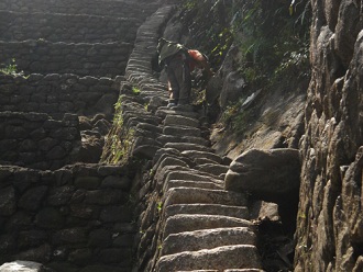 Bajada de Huaynapicchu, escalera irregular
                    escarpada con turista a 4 patas, primer plano